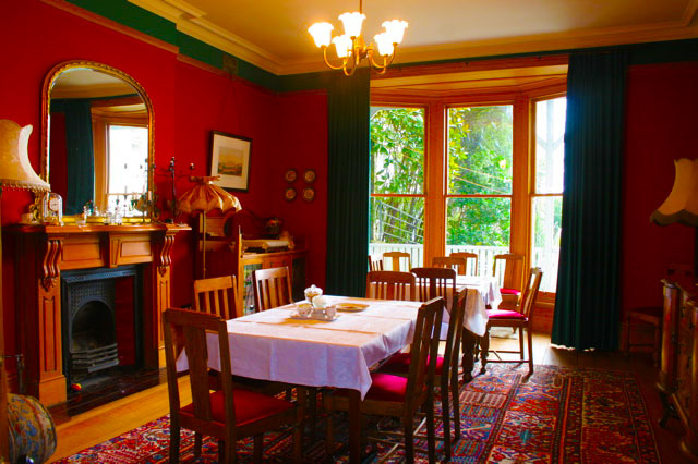The dining room at Braemar on Parliament Street, with red walls, a bay window and tables laid with white linen